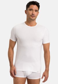 Hvid kortærmet t-shirt lavet af glat stof med en klassisk rund halsudskæring. Bæres med hvide tætsiddende trusser, der viser et sømløst design.