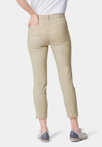 Beige broek met hoge taille en een aansluitend ontwerp. Bevat twee achterzakken en heeft een soepele textuur. Gepaard met grijze en witte schoenen.