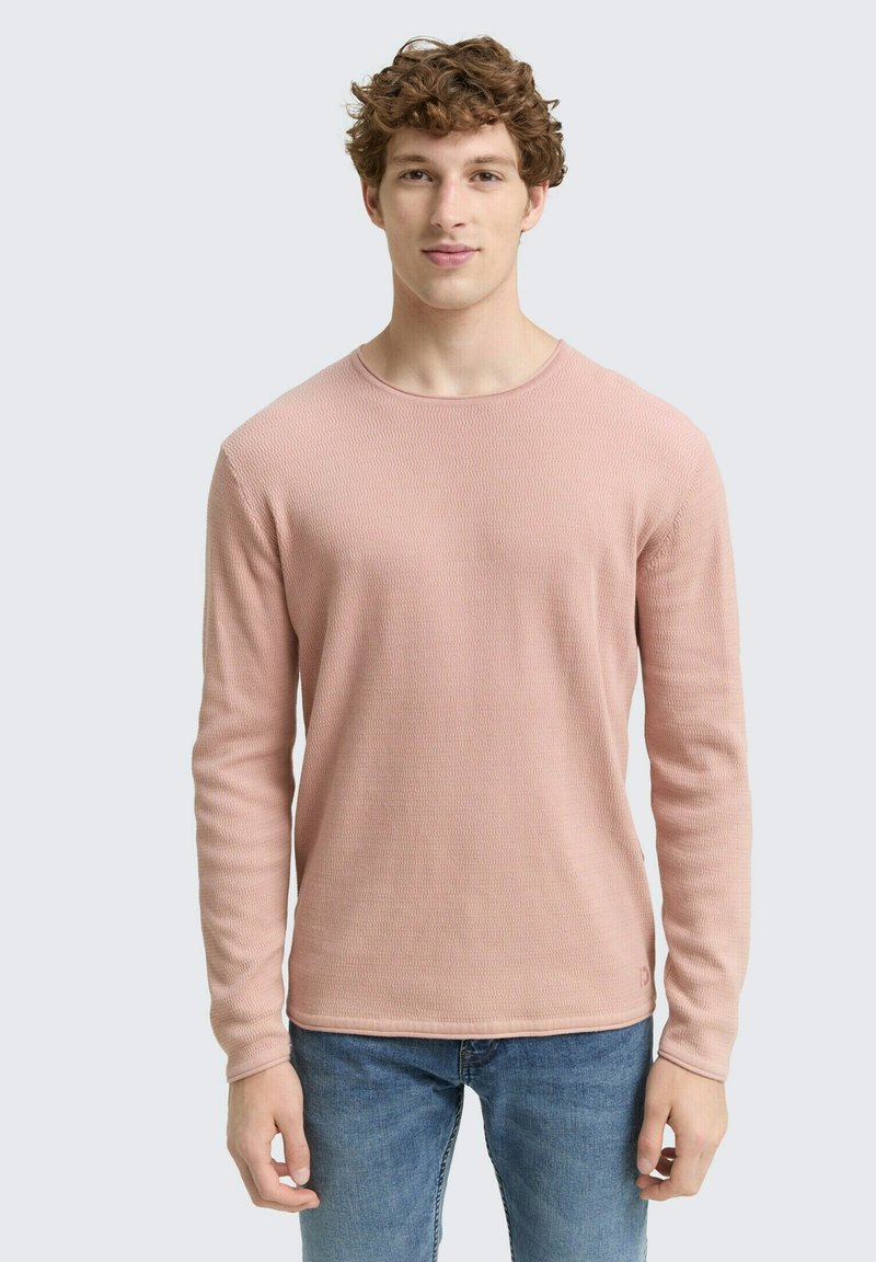 Langsleeve trui met ronde hals in een lichtroze, gestructureerde brei-stof. Een subtiele logo-accent op de linksonder. Gecombineerd met blauwe spijkerbroek.