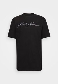 Černé bavlněné tričko s krátkým rukávem a kulatým výstřihem, na přední straně s bílým kurzívním logem "Karl Kani". Hladká textura.