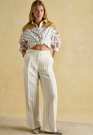 Košeľa s kvetinovým vzorom v žltej a bielej farbe, zviazaná v páse; široké krémové nohavice s tenkými zvislými pruhmi; mäkká látka.
