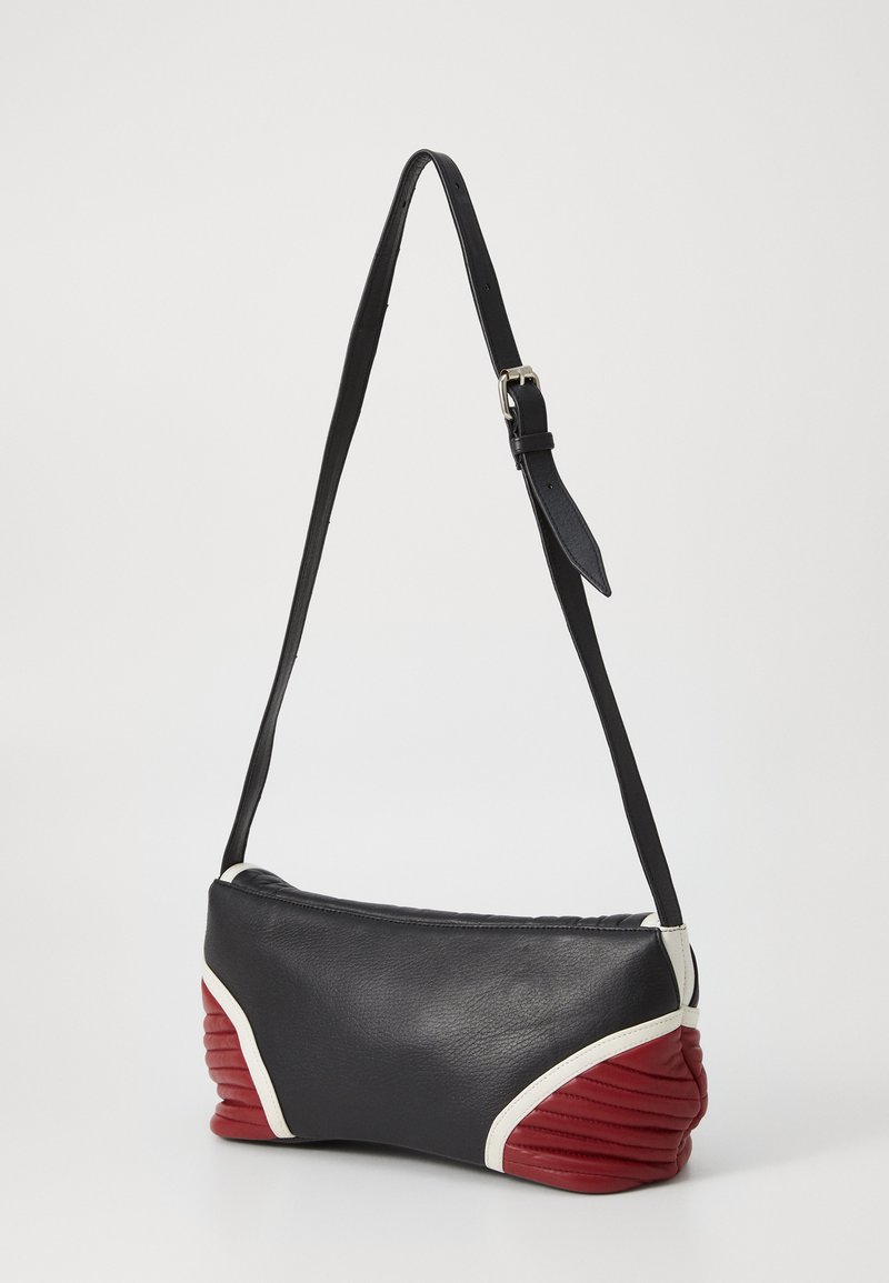 Schwarze Lederhandtasche mit einem strukturierten roten Akzent am Boden, ausgestattet mit einem verstellbaren Gurt und einer glatten Oberfläche. Weiße Paspelierung.