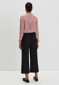 Rode en witte gestreepte blouse met knopen en een rugplooi, gecombineerd met zwarte brede broek en zwarte flats. Glad textuur van de stof.