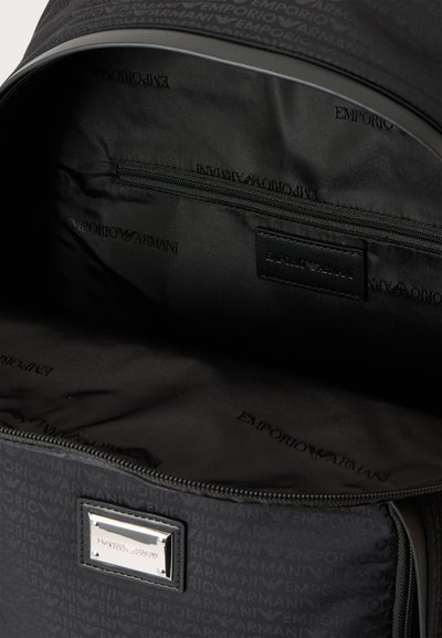 Sac à dos Emporio Armani noir ouvert avec doublure en tissu siglé, poche intérieure zippée et plaque métallique avec logo à l’avant.