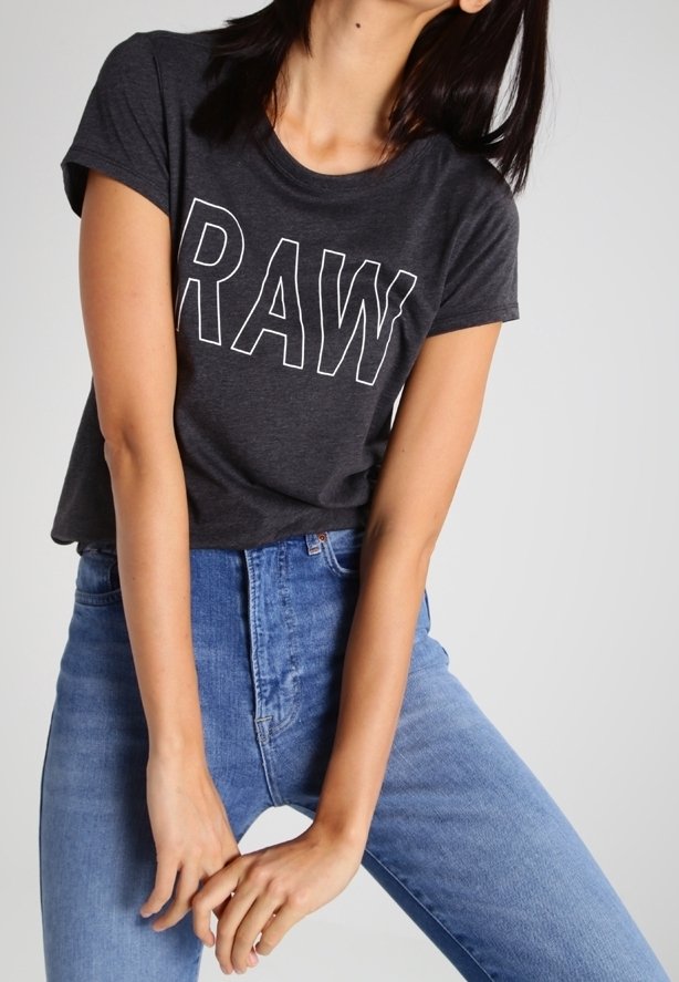 T-shirt gris foncé avec "RAW" imprimé en lettres blanches. Manches courtes, col rond, associé à un jean taille haute bleu clair.