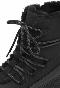 Botte en similicuir noir avec une doublure intérieure en peluche, lacets noirs épais avec des accents gris, col rembourré et semelle texturée.