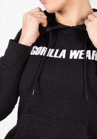 Zwarte hoodie van gemengde katoen, met een voorzak, verstelbaar koord en grote witte tekst "GORILLA WEAR" over de borst.