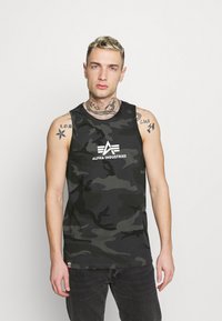 Čierny a šedý maskáčový tielko s okrúhlym výstrihom a bielym logom "Alpha Industries" na prednej strane. Tkanina má hladkú textúru.