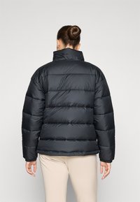 Zwarte pufferjack met hoge kraag, voorzien van gewatteerde vulling, elastische manchetten en een neutrale achtergrond.