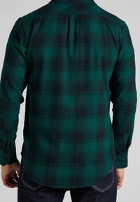 Groen en zwarte geruite flanellen shirt met lange mouwen, knoopmanchetten en een afgeronde zoom. Heeft een yoke op de bovenrug voor extra structuur.