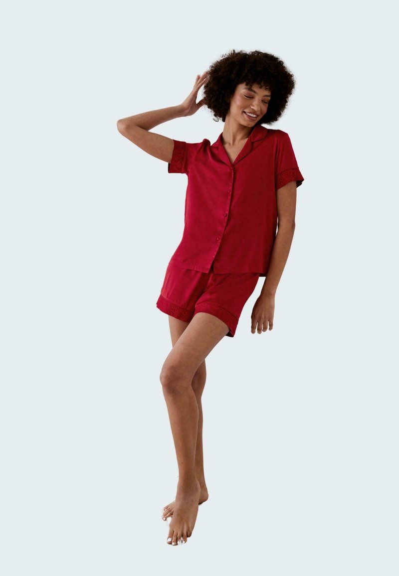Red short-sleeve pajama set featuring a button-up top with lace cuff accents and matching shorts with lace trim. Smooth fabric texture.