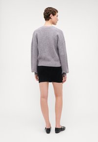 Harmaa neulepaita, jossa on roikkuvat olkapäät, ribbireunukset ja helma. Yhdistetty mustaan farkkuhameeseen ja mustiin tasapohjaisiin kenkiin. Minimalistinen muotoilu.