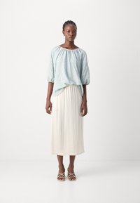 Lys blå strukturert bluse med innsamlet hals, paret med en flytende, kremfarget ankel-length skjørt og nude sandaler med remmer.