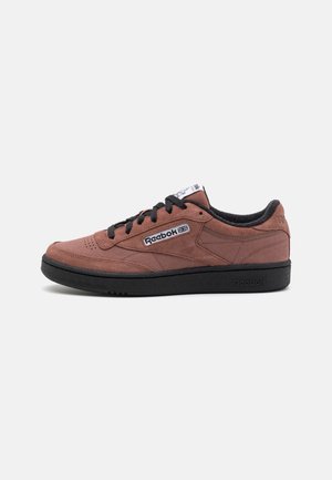 Brun ruskind Reebok sneaker med sort sål og snørebånd, Reebok logo på siden og tungen, vist i venstre profil på hvid baggrund.
