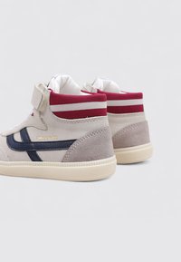 Zapatillas altas de ante beige con una franja azul marino. Presentan acentos en burdeos y cuellito acolchado, con suela de goma suave en color crema.