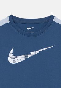 Μπλε αθλητική μπλούζα με στρογγυλή λαιμόκοψη. Διαθέτει μεγάλο λευκό λογότυπο της Nike με ψηφιοποιημένο σχέδιο. Τα μανίκια είναι από ανοιχτό μπλε ύφασμα με δυαδρό διάτρημα.