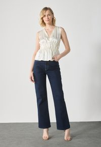 Un haut en satin blanc avec un décolleté en V et une taille froncée, associé à un jean noir large. Des sandales à talons neutres complètent la tenue.