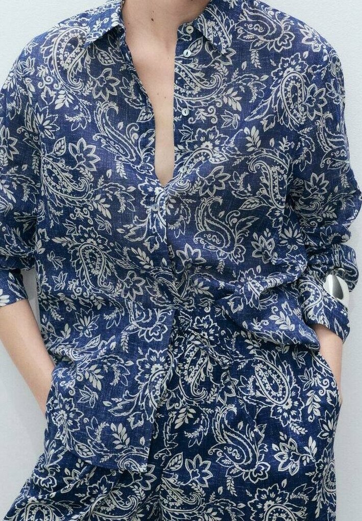 Personne portant une chemise à manches longues et un pantalon assorti à motif cachemire bleu et blanc, les mains dans les poches, visage non visible.