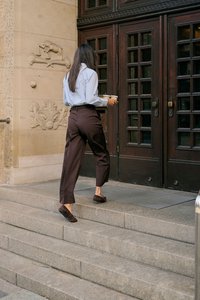 Femme portant deux tasses de café marchant sur des marches en pierre vers de grandes portes doubles en bois d'un bâtiment aux murs en pierre sculptée.
