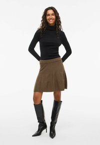 Pull à col roulé noir, jupe en tricot A-line marron, et bottes en cuir noires à talons hauts ; modèle se tenant avec les mains sur les hanches.
