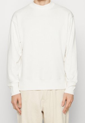 Weißer Pullover mit hohem Ausschnitt und langen, weiten Ärmeln. Hergestellt aus weichem Baumwollstoff, mit geripptem Saum und Bündchen.