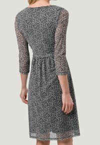 Vestido con estampado floral en blanco y negro, con mangas transparentes de tres cuartos, cintura ajustada y falda plisada, fabricado en tela ligera.