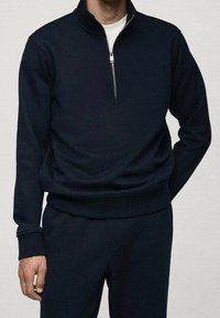 Pullover blu navy con zip e collo alto, realizzato in tessuto liscio, con maniche lunghe, polsini a coste e un design leggero.