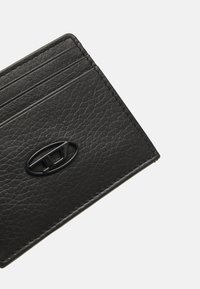 Cartera de piel negra con acabado texturizado, múltiples compartimentos para tarjetas y un acento en forma de óvalo prominente en el frontal.