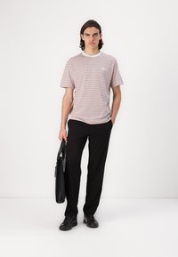 Striped T-shirt in light red and white, with a crew neck and logo detail on the chest, paired with black trousers and black shoes.