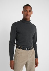 Maglione a collo alto grigio scuro in morbido tessuto, abbinato a pantaloni in velluto a coste beige chiaro e una cintura nera. Design semplice, silhouette aderente.