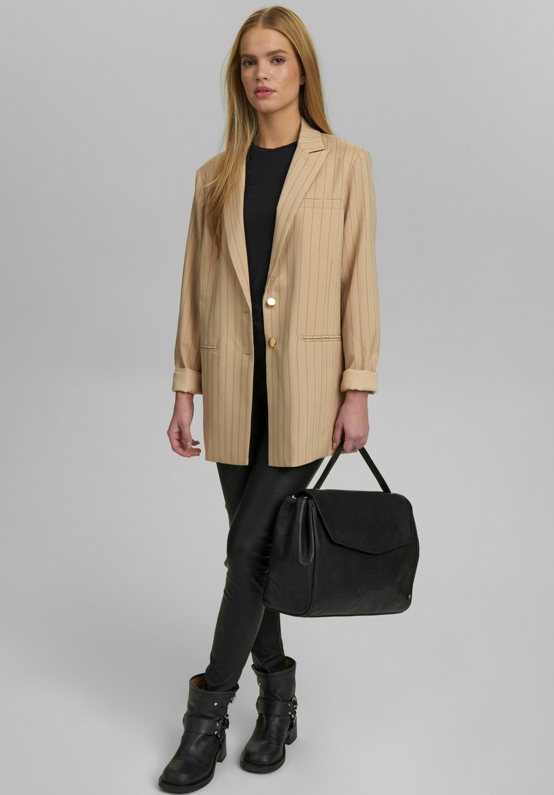 Beige randig kavaj med guldknapp, svart figurnära topp, svarta leggings och ankelboots. Svart handväska med strukturerad design.