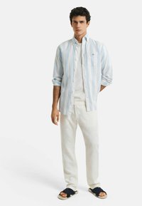 Lichtblauw en wit gestreepte blouse, witte T-shirt, witte broek en marineblauwe sandalen. Heeft een relaxte pasvorm en casual stijl.