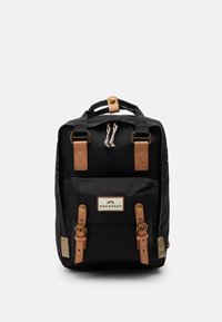 Black backpack with leather accents, featuring a top handle, adjustable straps, and a front pocket with a branded patch and decorative hardware.
