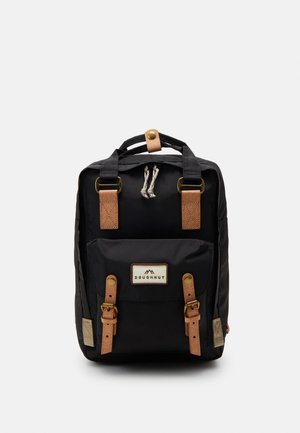 Black backpack with leather accents, featuring a top handle, adjustable straps, and a front pocket with a branded patch and decorative hardware.