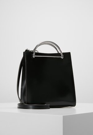 Bolso de mano de cuero negro con asas de arco de metal plateado y una correa de hombro desmontable, exhibido sobre un pedestal blanco contra un fondo claro.