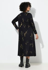 Pitkähihainen musta mekko, jossa on kultaiset roiskeet, slim fit -malli ylhäällä, virtaviivainen muotoilu, valmistettu pehmeästä kankaasta, yhdistetty mustiin nilkkasaappaisiin.