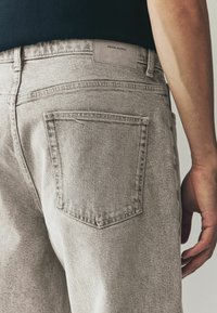 Lichtgrijze denim jeans met een subtiele textuur, voorzien van een achterzak en een merklabel op de tailleband. Tailored fit met strakke lijnen.