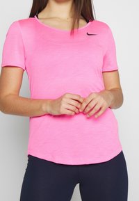 Rosa kortärmad idrottströja med rund halsringning, tillverkad av lättviktsmaterial, med en svart Nike swoosh-logotyp på bröstet.
