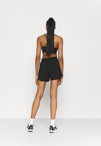 Conjunto atlético negro que incluye un sujetador deportivo ajustado y pantalones cortos de corte holgado. El material parece suave; incluye zapatillas deportivas y calcetines hasta los tobillos.