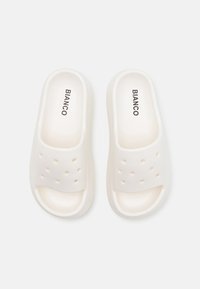 Witte instapsandalen gemaakt van zacht materiaal met een gladde textuur, voorzien van perforaties op de band voor ventilatie en comfort.