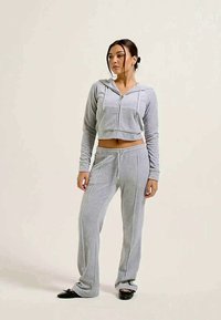 Conjunto acinzentado composto por um hoodie cropped com fecho e calças com cordão. Tecido suave com uma textura lisa e discretos detalhes em piping lateral.