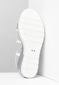 White sandal with a textured rubber sole and gray accents. Features adjustable straps and a smooth upper surface. Made in Italy.