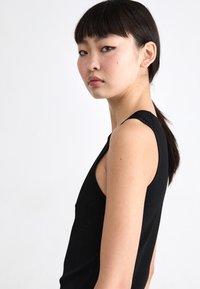 Zwarte mouwloze top met een getailleerd design, voorzien van brede schouderbanden en een gladde textuur, getoond op een model in profiel.
