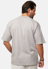 Graues Baumwoll-T-Shirt mit kurzen Ärmeln und lockerer Passform. Mit Rundhalsausschnitt und glatter Textur, die das Design auf der Rückseite hervorhebt.