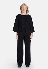 Top nero con dettaglio anteriore annodato e maniche larghe, abbinato a pantaloni neri a gamba larga. Tessuto morbido e design monocromatico.