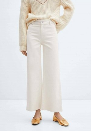 Bredde-beige denimbukser med rå kant, parret med en tekstureret beige sweater og gyldne slip-on sko.