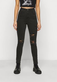 Jeans ajustados negros con desgastes en las rodillas, diseño de cintura alta y una textura suave y gruesa. Combinados con botas negras con cordones.