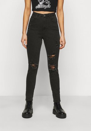 Jeans ajustados negros con desgastes en las rodillas, diseño de cintura alta y una textura suave y gruesa. Combinados con botas negras con cordones.