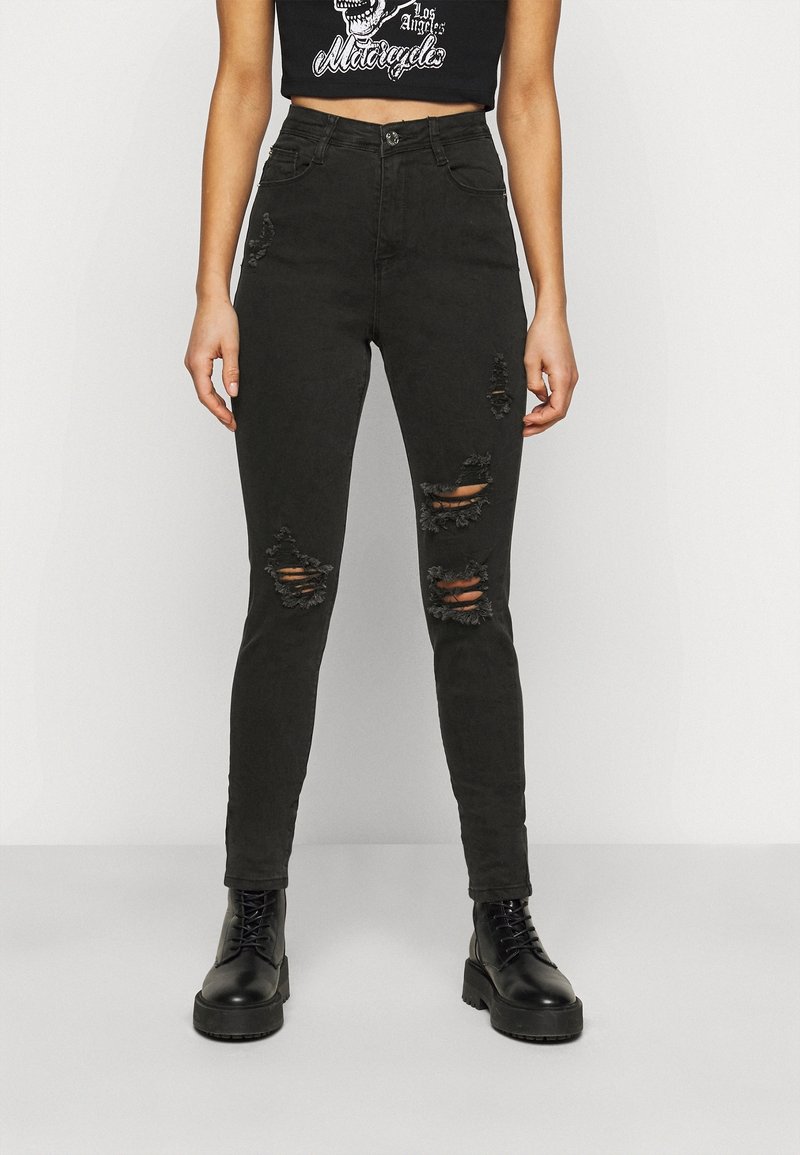 Jeans ajustados negros con desgastes en las rodillas, diseño de cintura alta y una textura suave y gruesa. Combinados con botas negras con cordones.