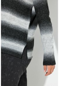 Musta ja harmaa liukuvärjätty neulepaita, pehmeällä neulostekstuurilla, resoreilla hihoissa ja sivuilla halkiot, yhdistetty tummiin kuvioituihin housuihin.